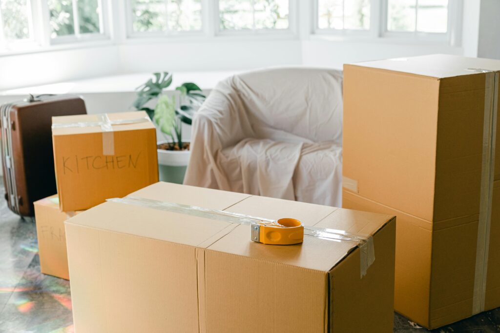 Cardboard boxes labeled 'Kitchen' in sunlit living room, ready for relocation.