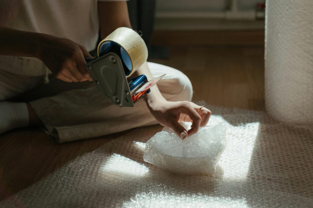 Close-up of a person preparing a package using bubble wrap and tape, indoors.