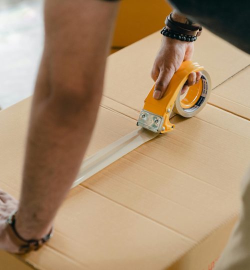 Man using packing tape to seal a cardboard box indoors. Ideal for moving or shipping concepts.