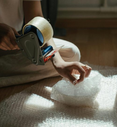 Close-up of a person preparing a package using bubble wrap and tape, indoors.